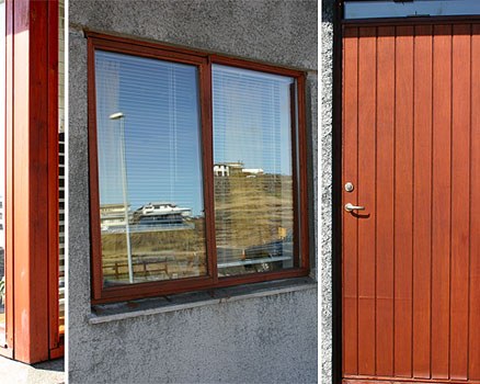 Gluggi í viðarramma og útihurð úr lóðréttum borðum.